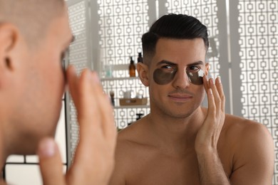 Photo of Man applying dark under eye patch near mirror at home