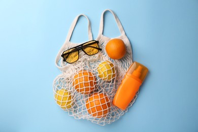 String bag with sunglasses, fruits and sunscreen on light blue background, flat lay