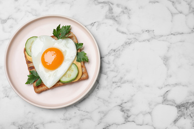 Plate of tasty sandwich with heart shaped fried egg on white marble table, top view. Space for text