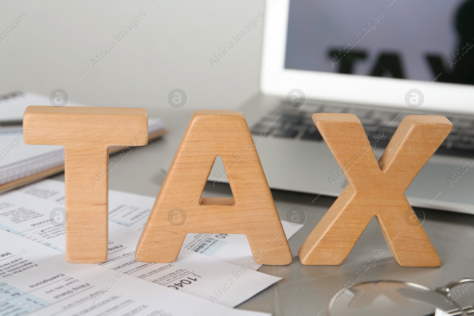 Photo of Word Tax made of wooden letters and documents near laptop on grey table, closeup