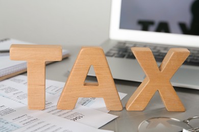 Word Tax made of wooden letters and documents near laptop on grey table, closeup