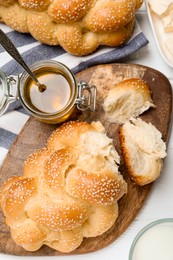 Photo of Homemade braided bread with sesame seeds, butter and honey on white wooden table, flat lay. Traditional challah