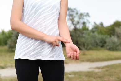 Photo of Young woman checking pulse after training in park, closeup