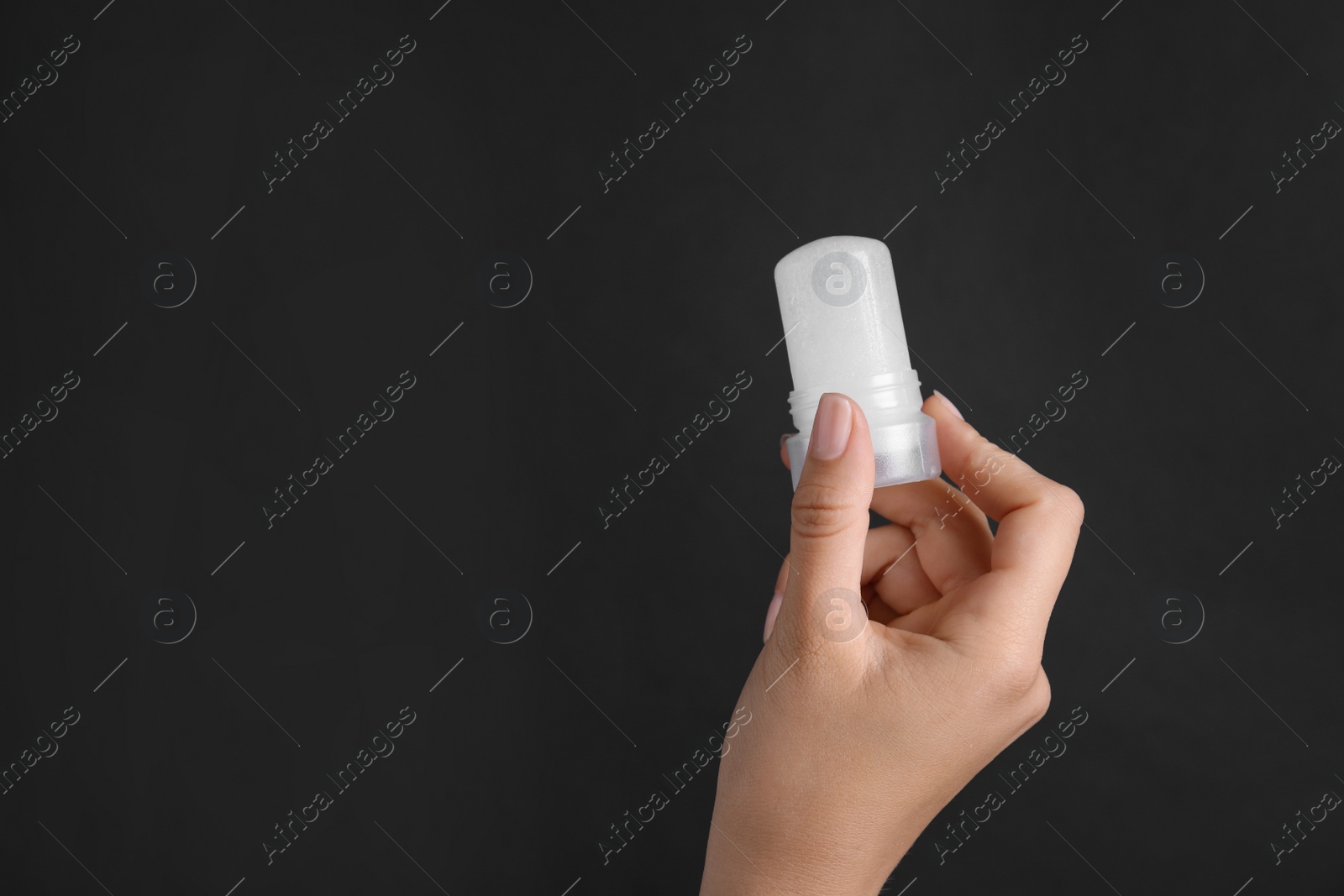 Photo of Young woman holding natural crystal alum deodorant on black background, closeup. Space for text