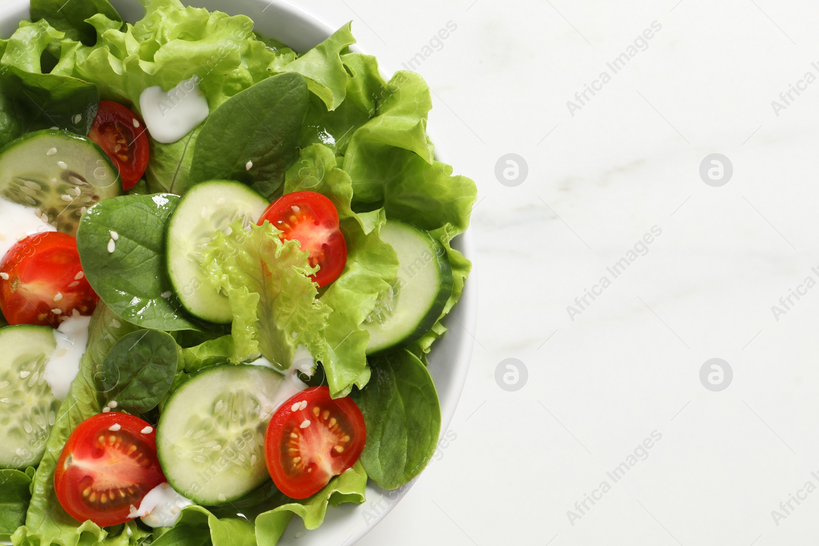 Photo of Delicious salad in bowl on white marble table, top view
