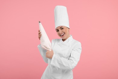 Happy professional confectioner in uniform holding piping bag on pink background