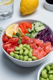 Photo of Poke bowl with salmon, edamame beans and vegetables on white table