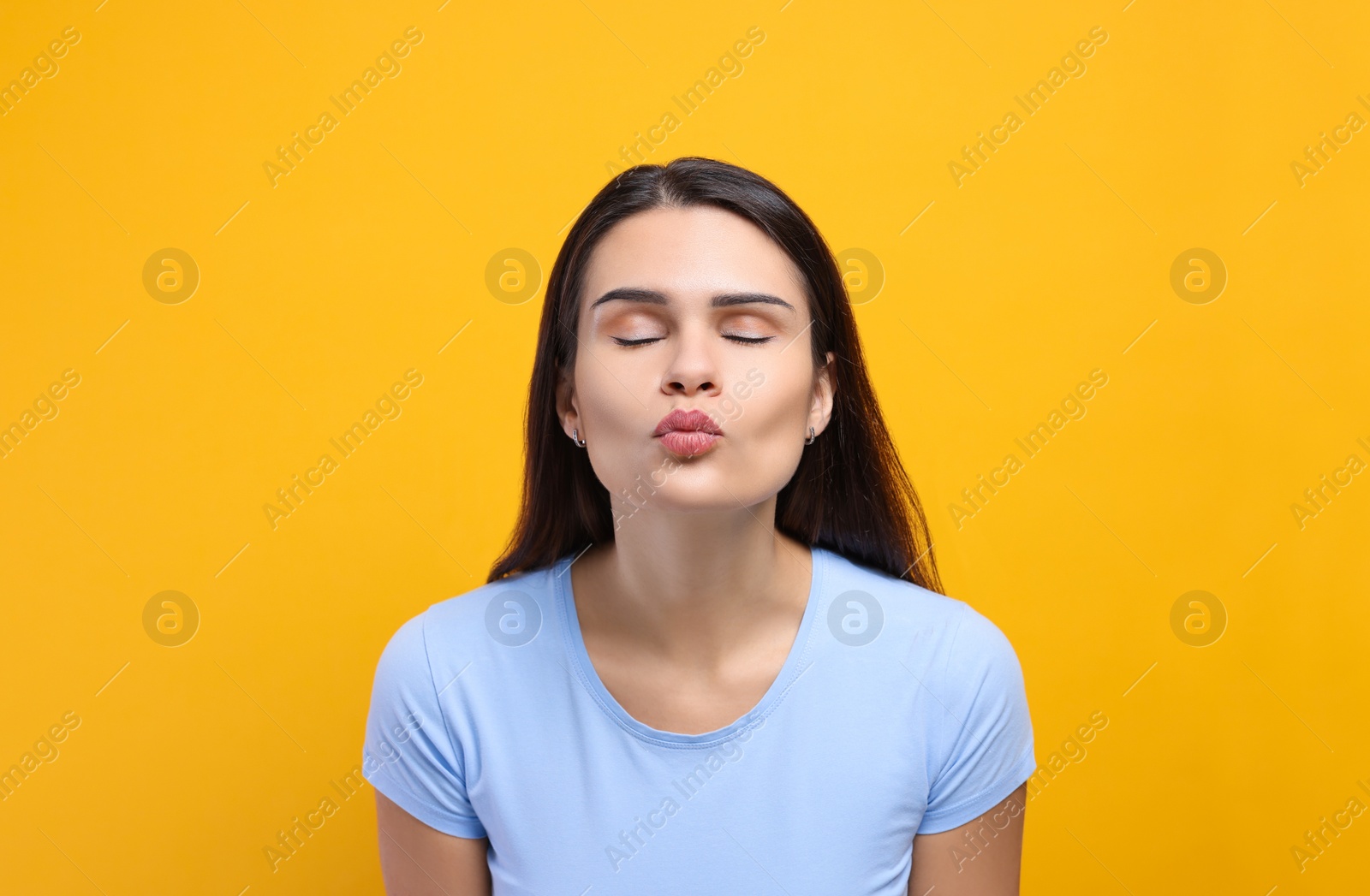 Photo of Beautiful young woman giving kiss on yellow background
