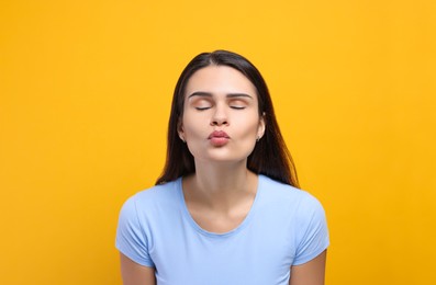 Beautiful young woman giving kiss on yellow background