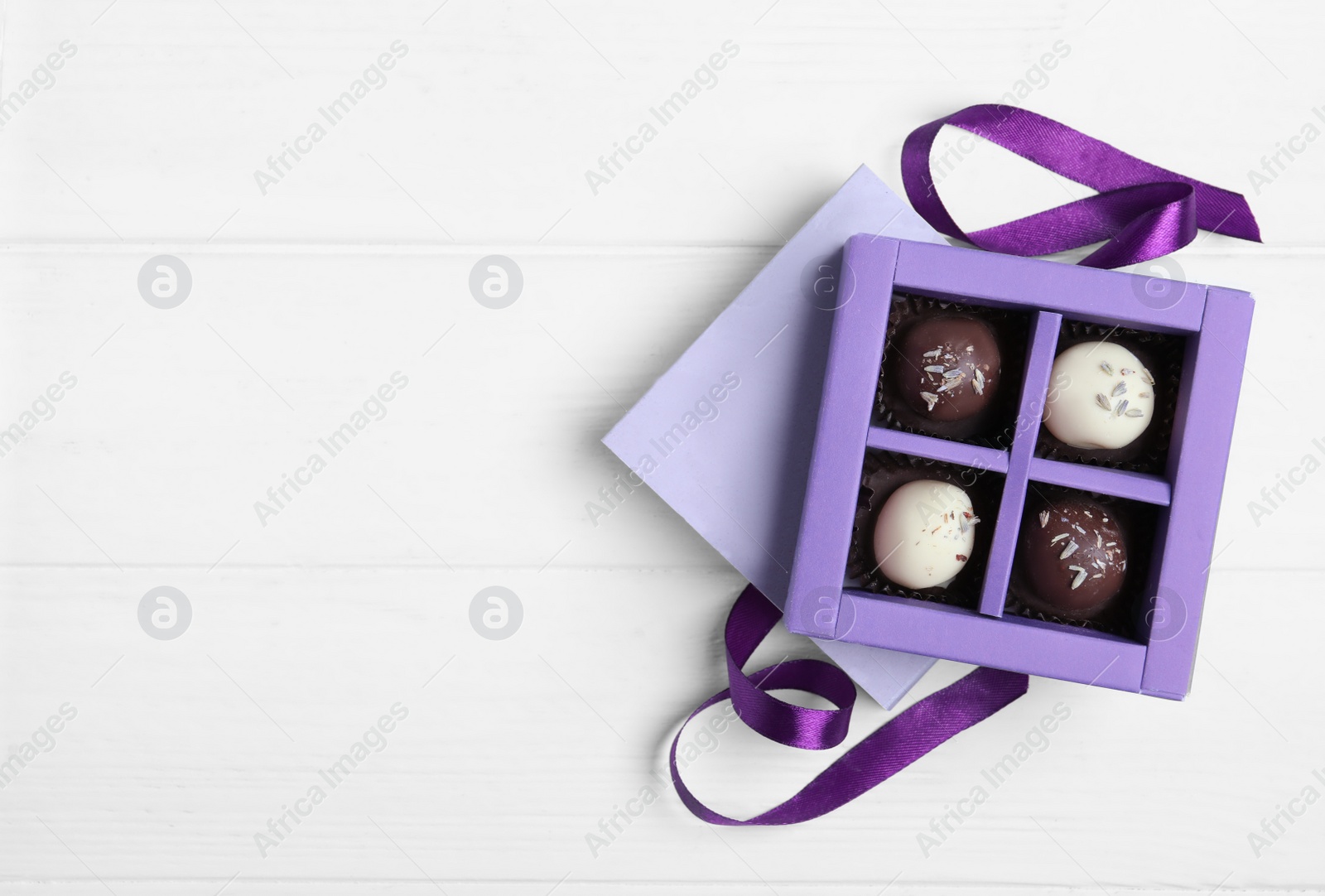 Photo of Box with tasty chocolate candies on white wooden table, flat lay. Space for text