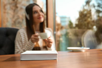 Photo of Book on table in cafe and woman with headphones on background. Audiobook concept