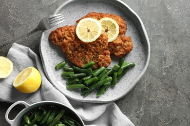 Photo of Tasty schnitzels served with lemon and green beans on grey table, flat lay