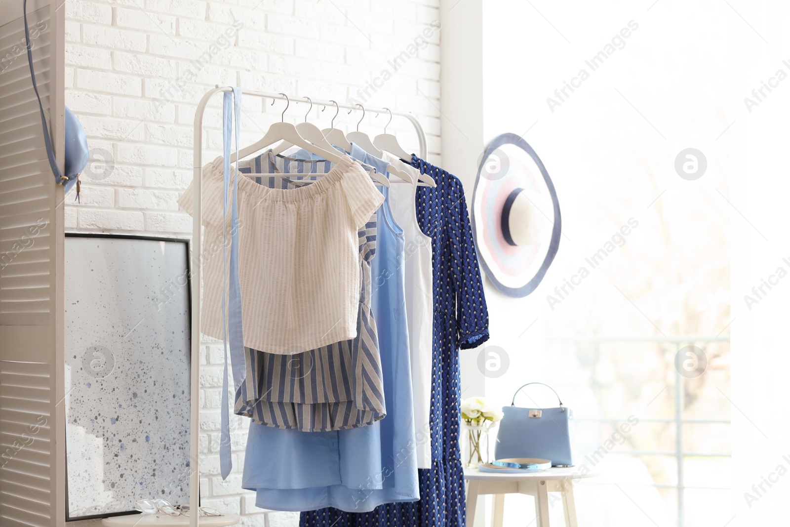 Photo of Wardrobe rack with women's clothes at white brick wall in room