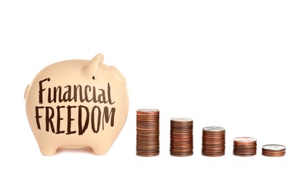 Image of Piggy bank with words Financial Freedom and stacked coins on white background