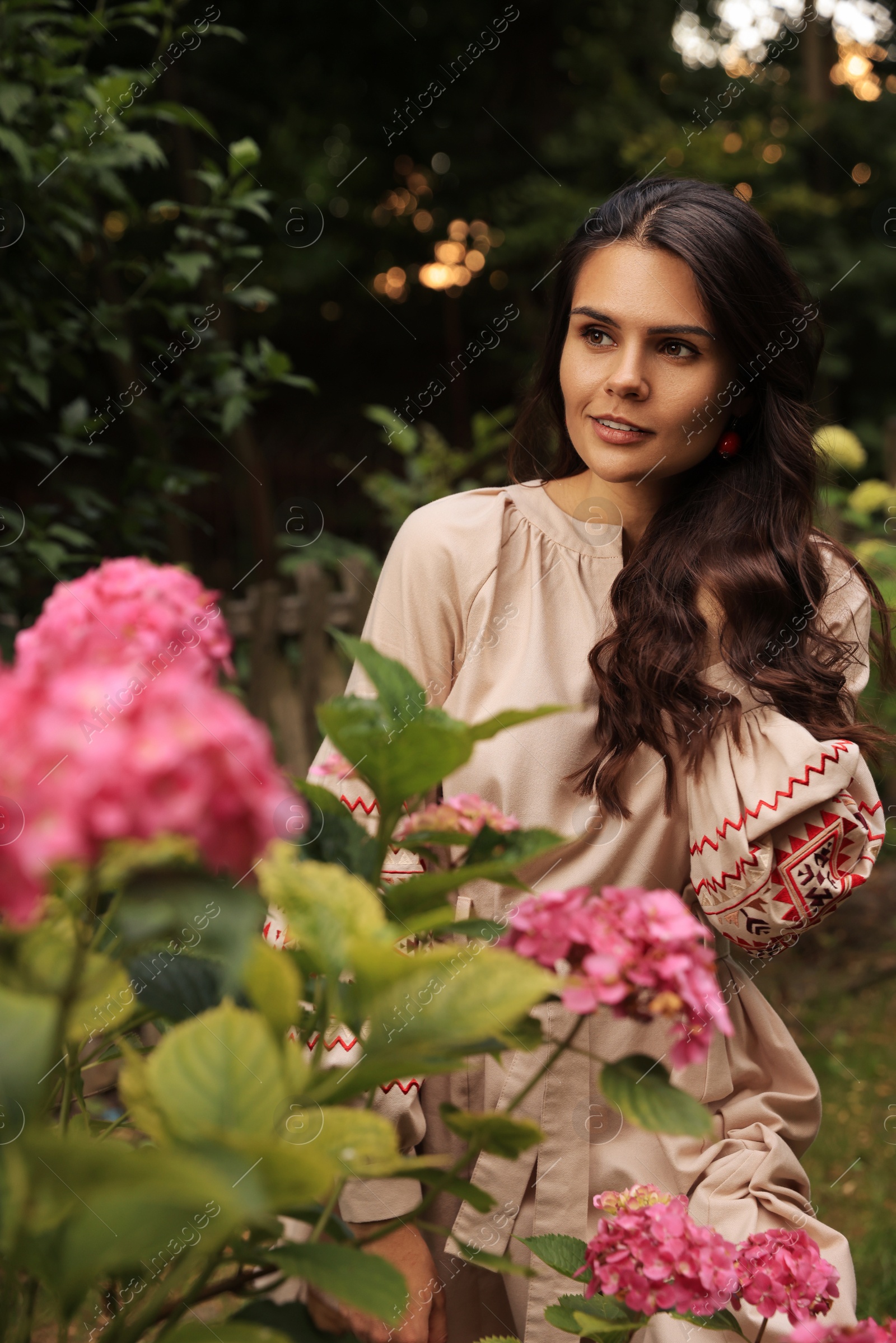 Photo of Beautiful woman wearing embroidered dress in blooming garden. Ukrainian national clothes