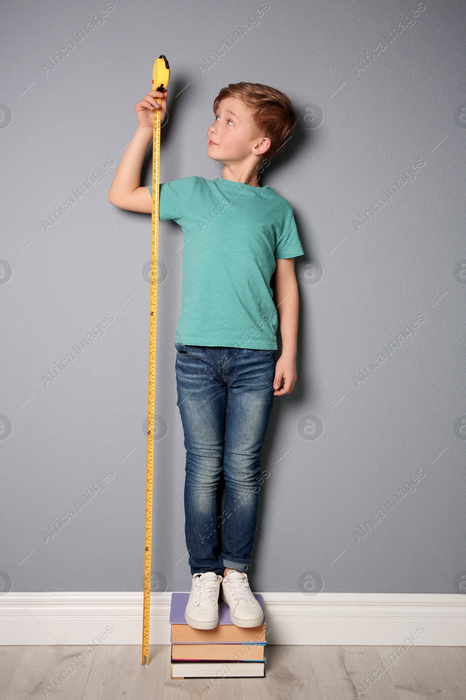 Photo of Little boy measuring his height near grey wall