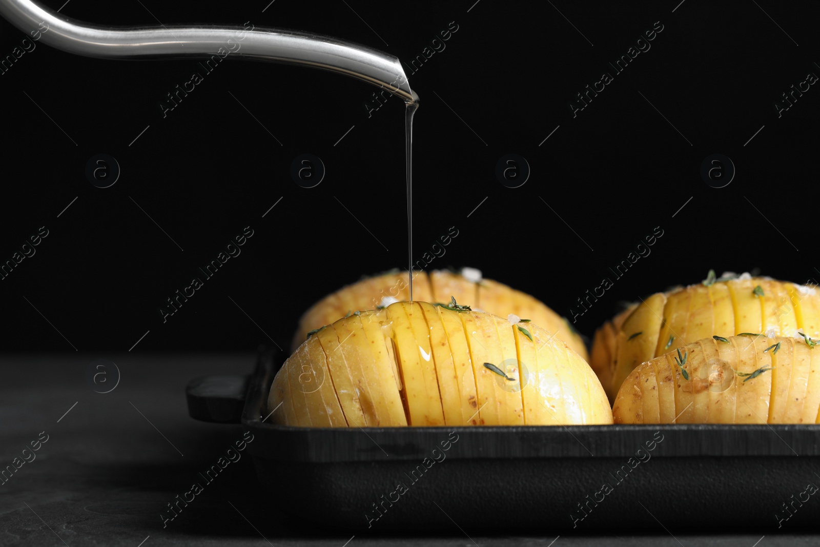 Photo of Oiling raw Hasselback potatoes before baking on dark grey table, closeup