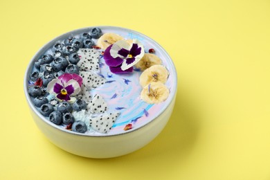 Delicious smoothie bowl with fresh fruits, blueberries and flowers on yellow background, closeup. Space for text