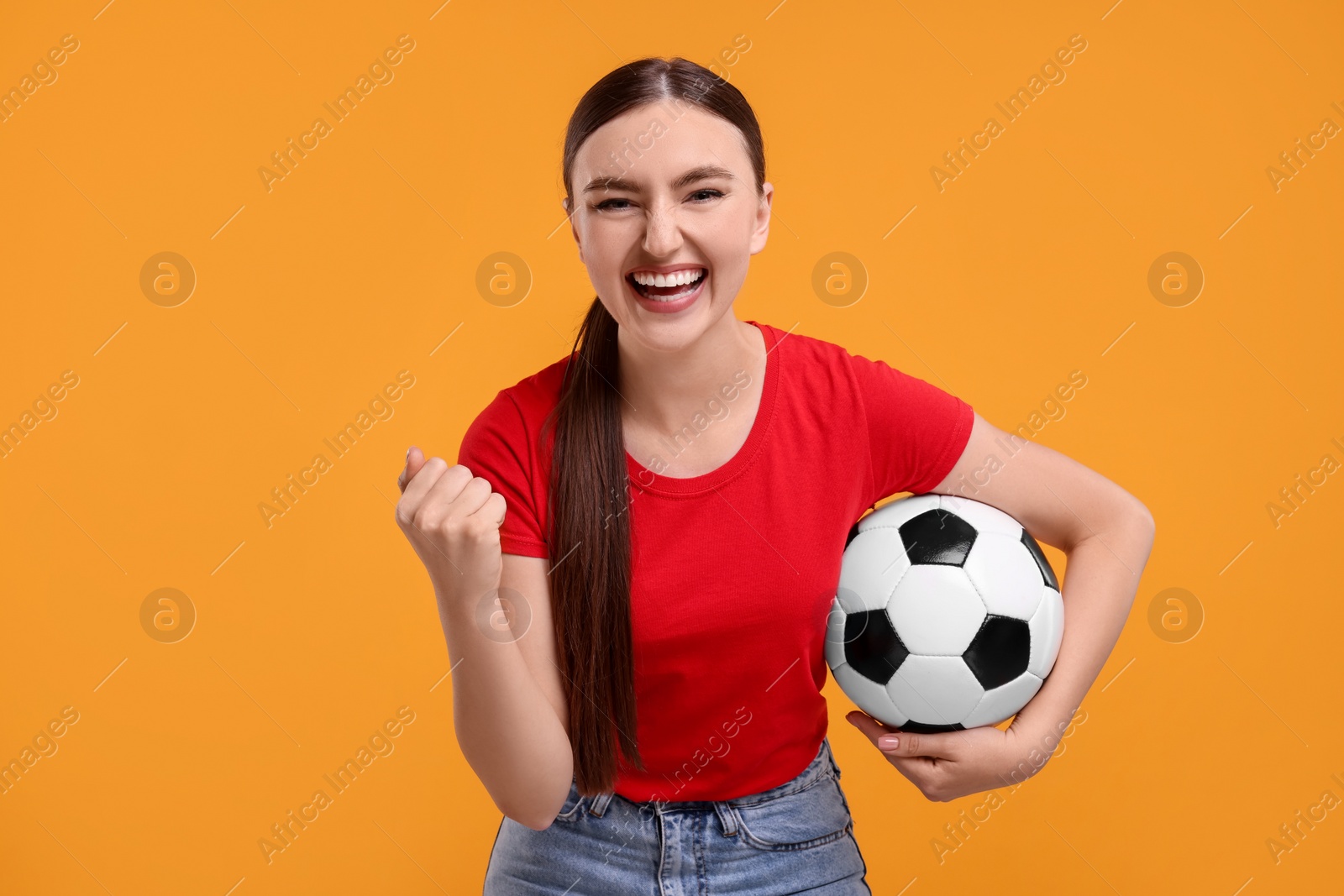 Photo of Happy soccer fan with ball celebrating on orange background