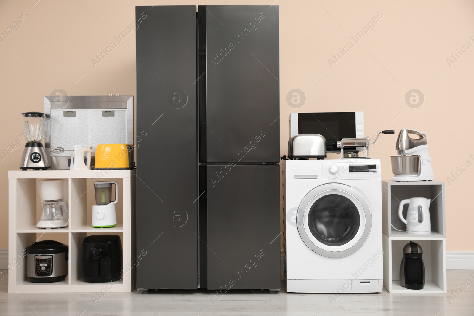 Photo of Modern refrigerator and other household appliances near beige wall indoors