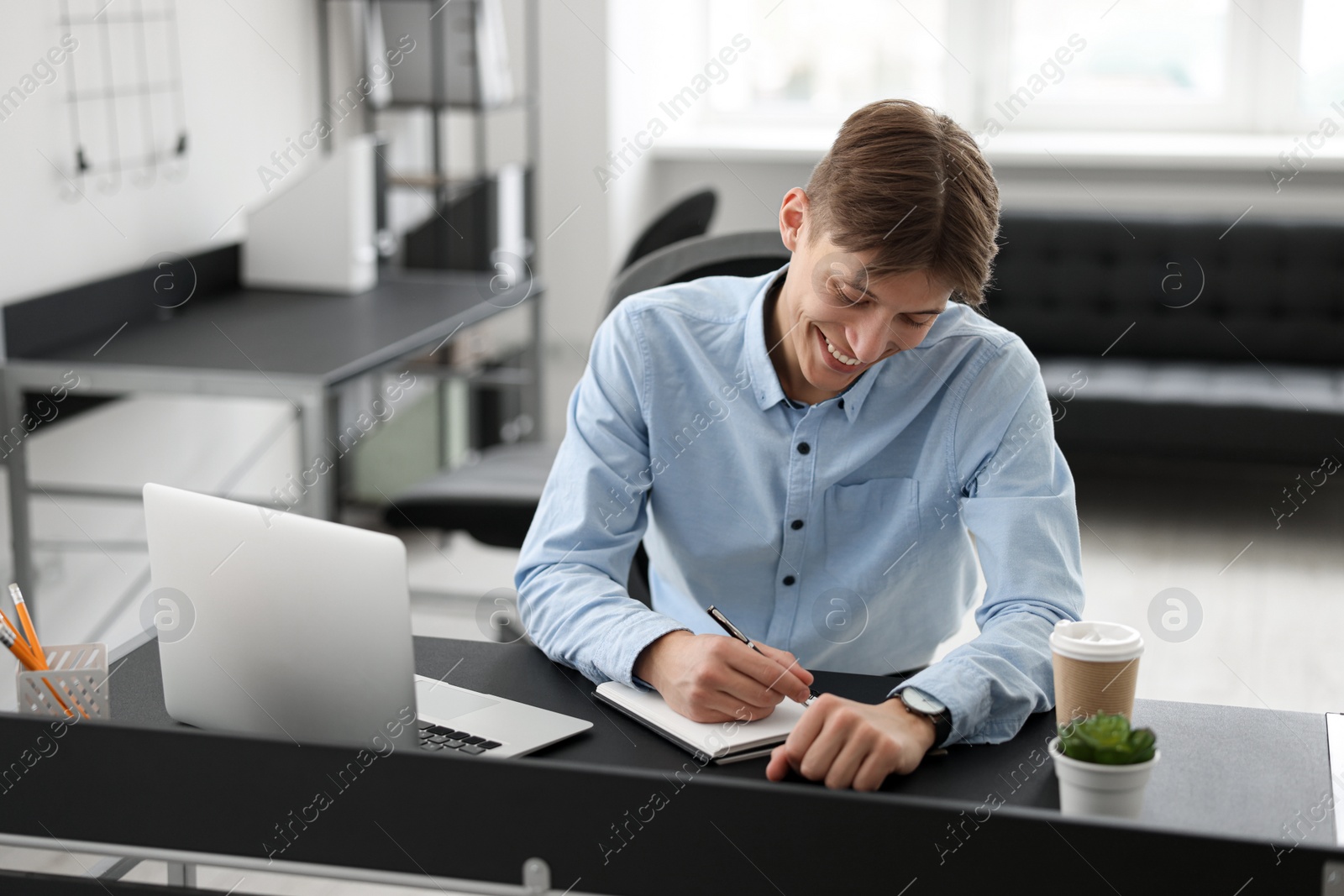 Photo of Man taking notes during webinar at table in office