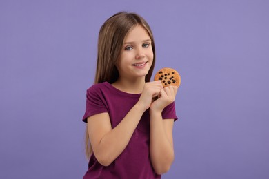 Cute girl with chocolate chip cookie on purple background