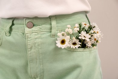 Photo of Woman with beautiful tender flowers in pocket of jeans on light background, closeup