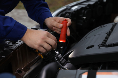 Mechanic with flashlight fixing car outdoors, closeup