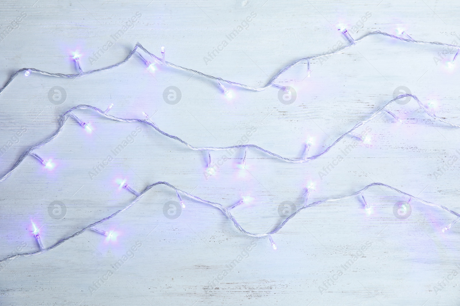 Photo of Glowing Christmas lights on wooden background, top view