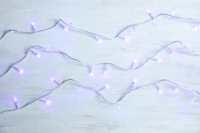 Photo of Glowing Christmas lights on wooden background, top view