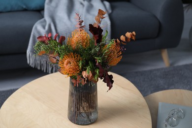 Photo of Vase with bouquet of beautiful leucospermum flowers, book and glasses on wooden nesting tables indoors