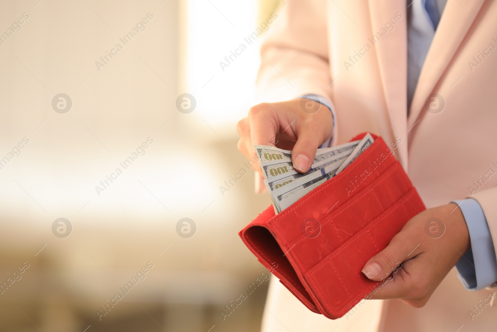 Photo of Young woman holding wallet with dollar bills on blurred background, closeup