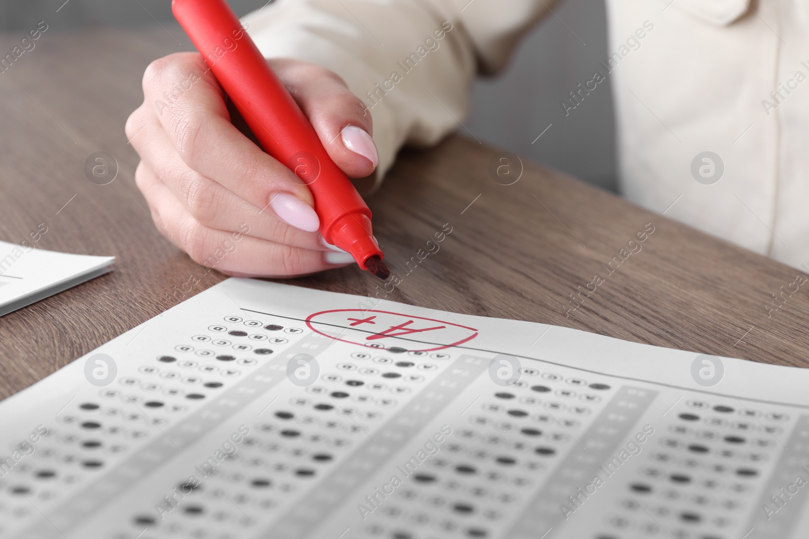 Photo of School grade. Teacher writing letter A with plus symbol on answer sheet at wooden table, closeup