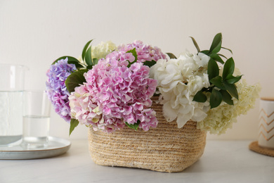 Photo of Beautiful hydrangea flowers in basket on light table, closeup