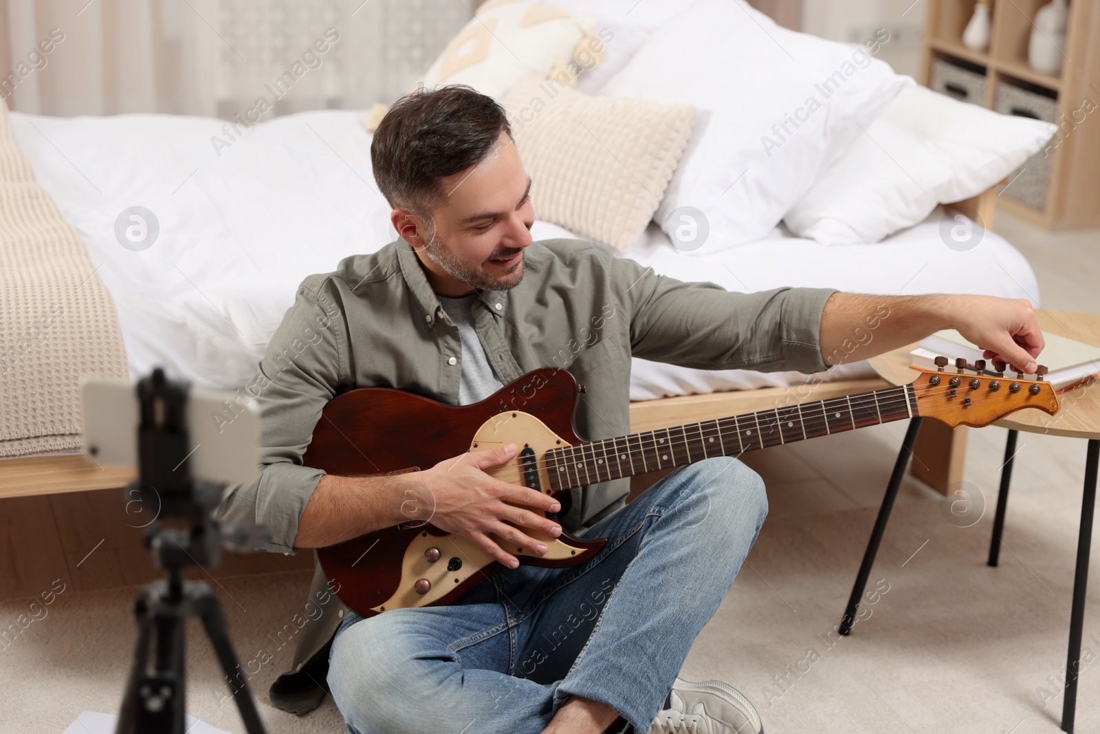 Photo of Music teacher tuning guitar while conducting online lesson at home. Time for hobby