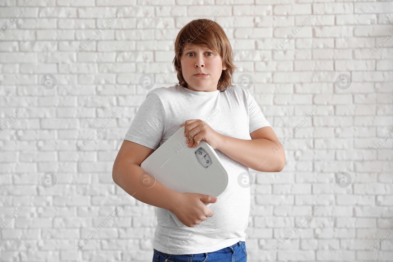 Photo of Emotional overweight boy with floor scales near white brick wall