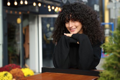 Photo of Happy young woman in stylish black sweater at wooden table outdoors, space for text