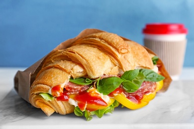 Photo of Tasty croissant sandwich with salami on table