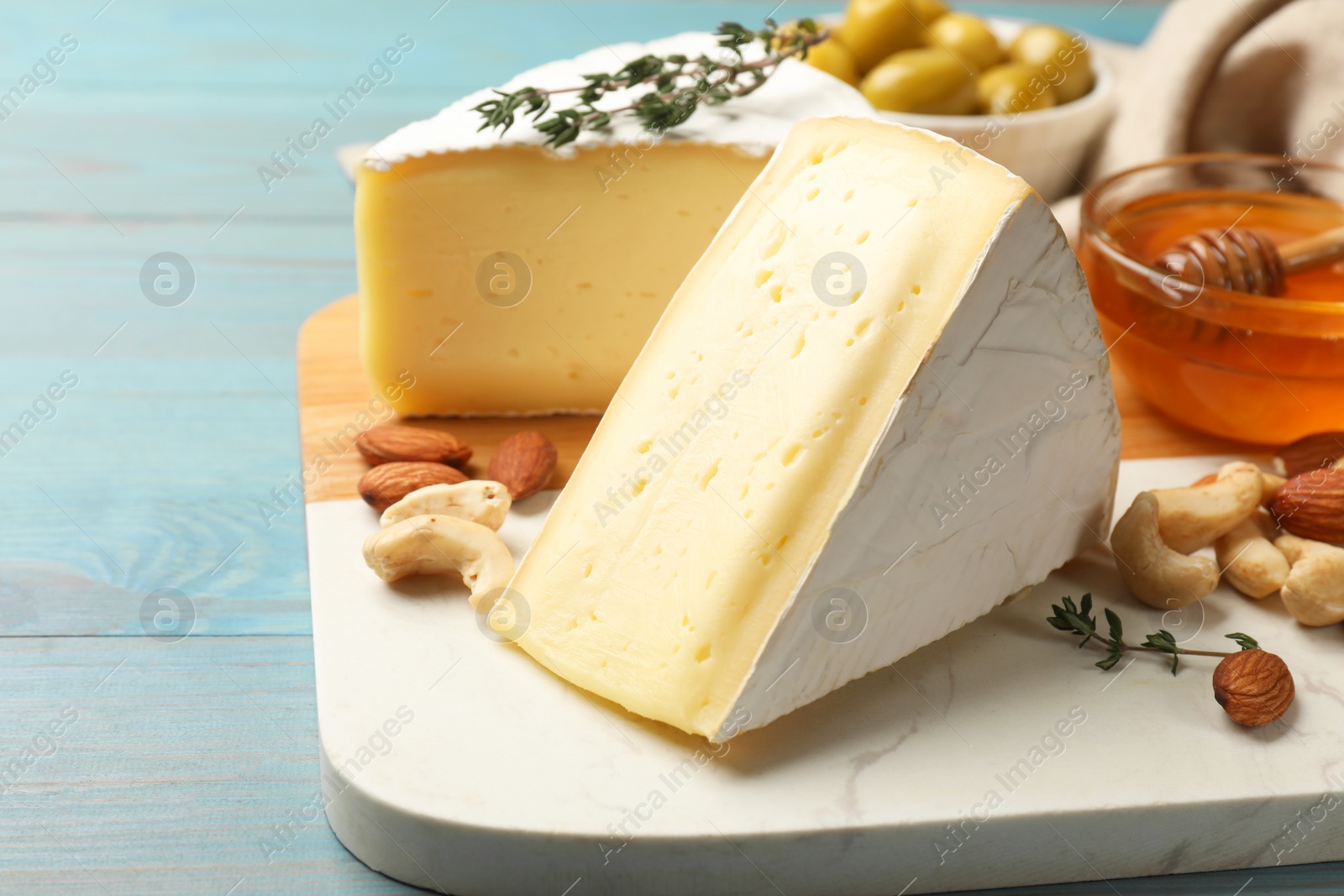 Photo of Tasty Camembert cheese with thyme, honey and nuts on light blue wooden table