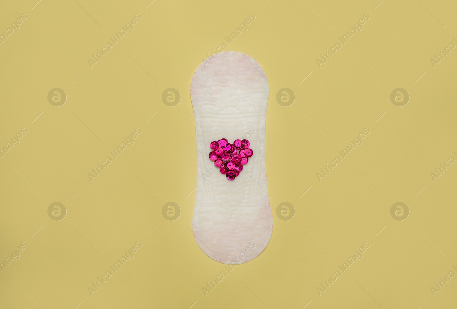 Photo of Sanitary pad with heart made of pink sequins on beige background, top view. Menstrual cycle