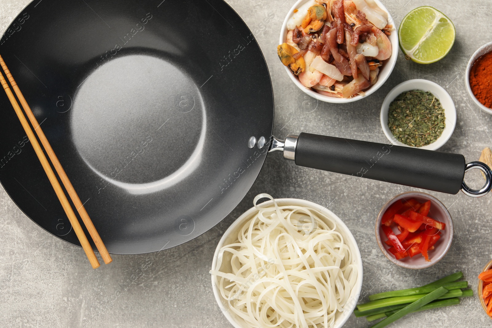 Photo of Flat lay composition with black wok, spices and products on grey textured table
