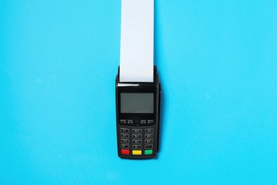 Photo of Payment terminal with thermal paper for receipt on light blue background, top view
