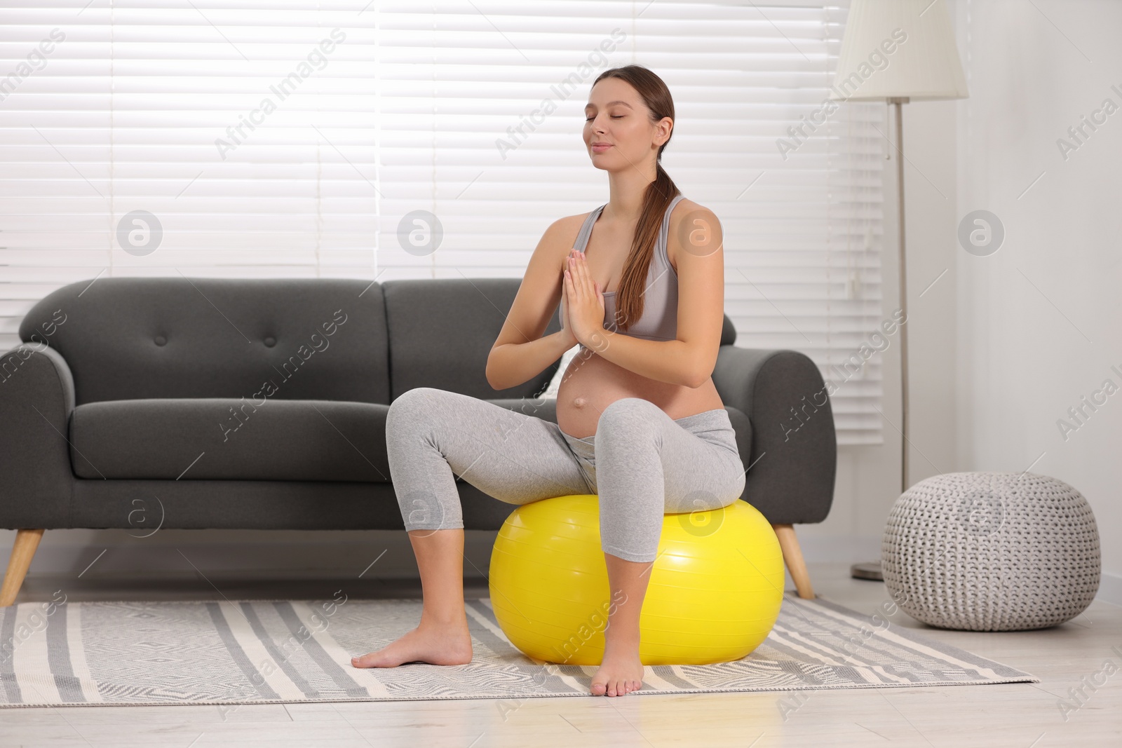 Photo of Pregnant woman meditating on fitness ball in room. Home yoga