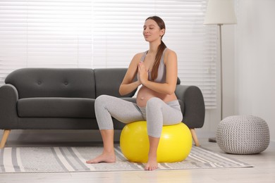 Pregnant woman meditating on fitness ball in room. Home yoga