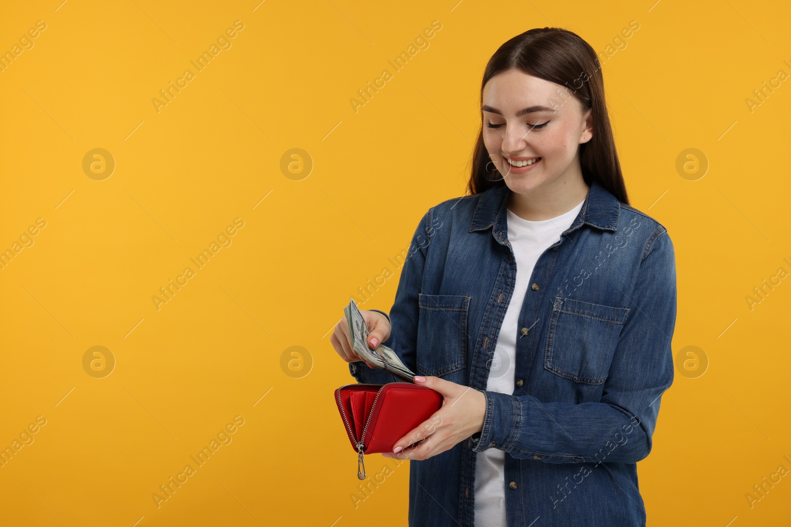 Photo of Happy woman putting money into wallet on orange background, space for text