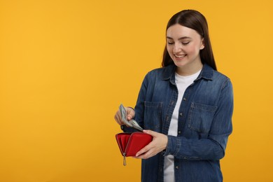 Happy woman putting money into wallet on orange background, space for text