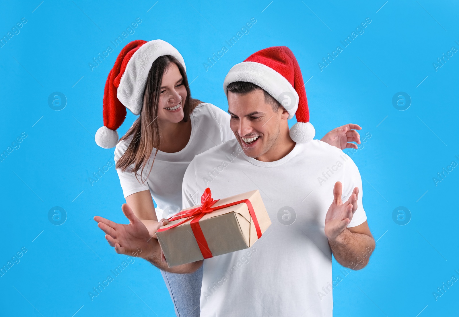 Photo of Woman presenting Christmas gift to boyfriend on light blue background
