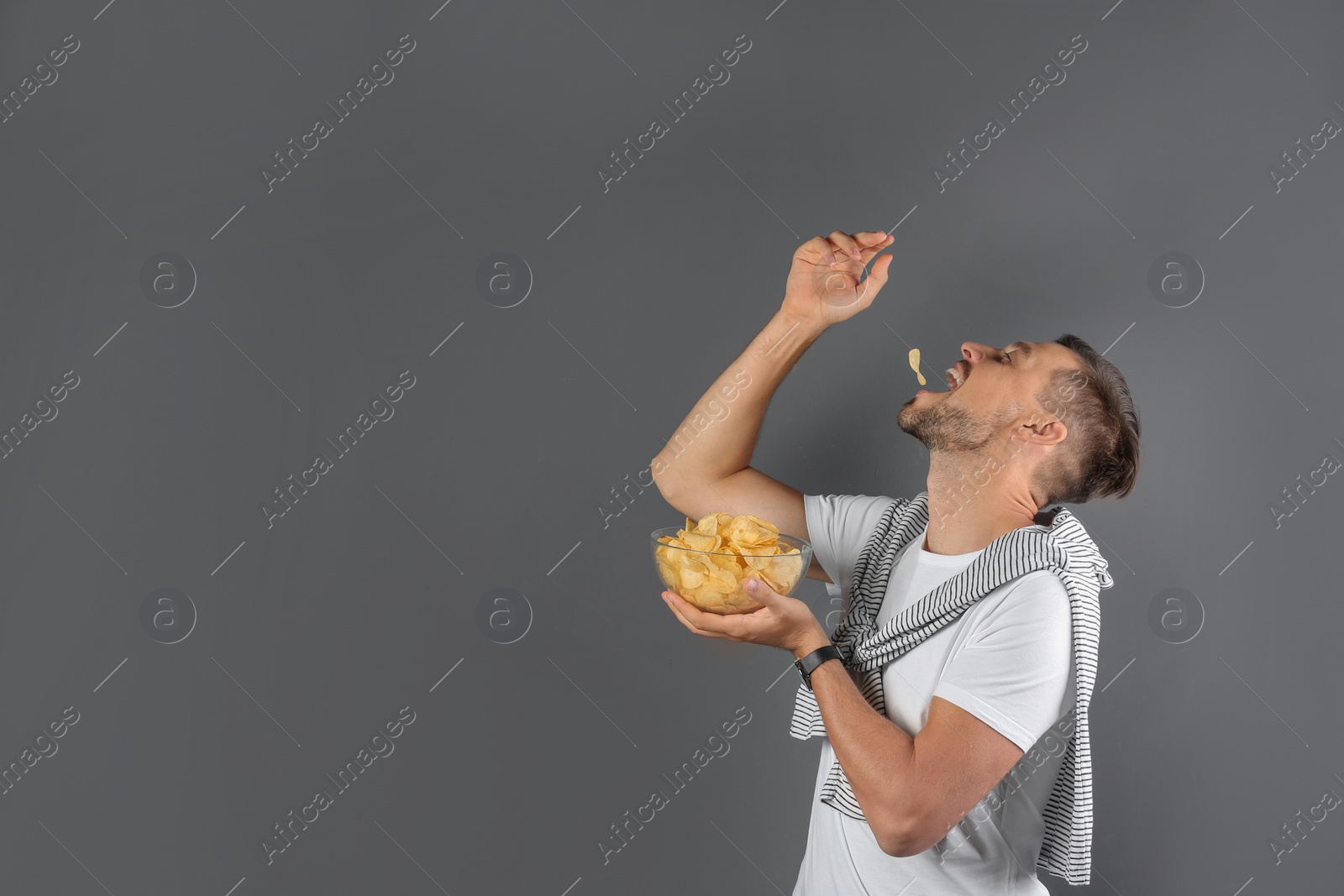 Photo of Man eating potato chips on grey background. Space for text