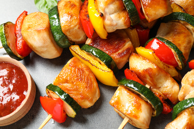 Photo of Delicious chicken shish kebabs with vegetables and ketchup on grey table, closeup
