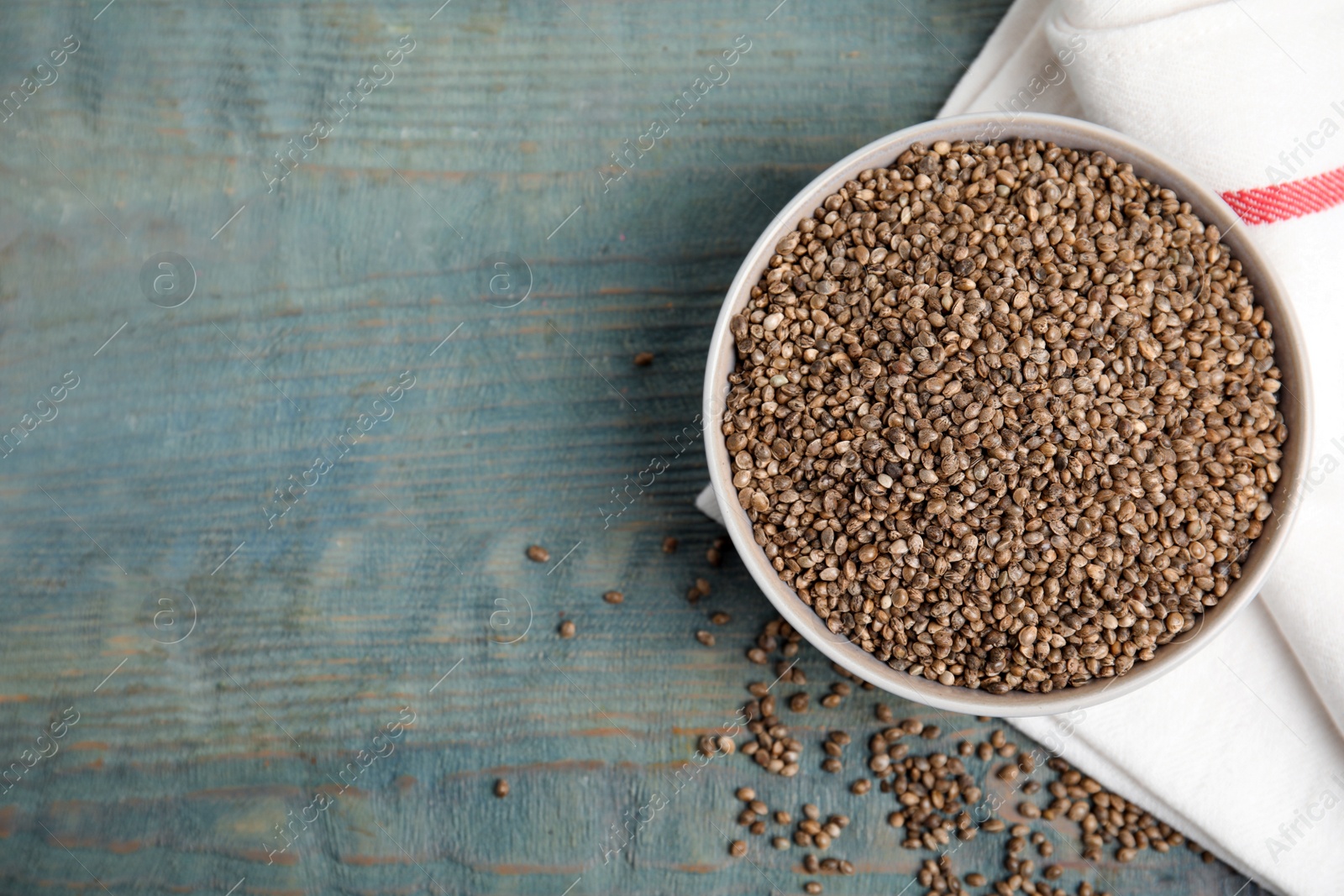 Photo of Bowl with organic hemp seeds on light blue wooden table, flat lay. Space for text